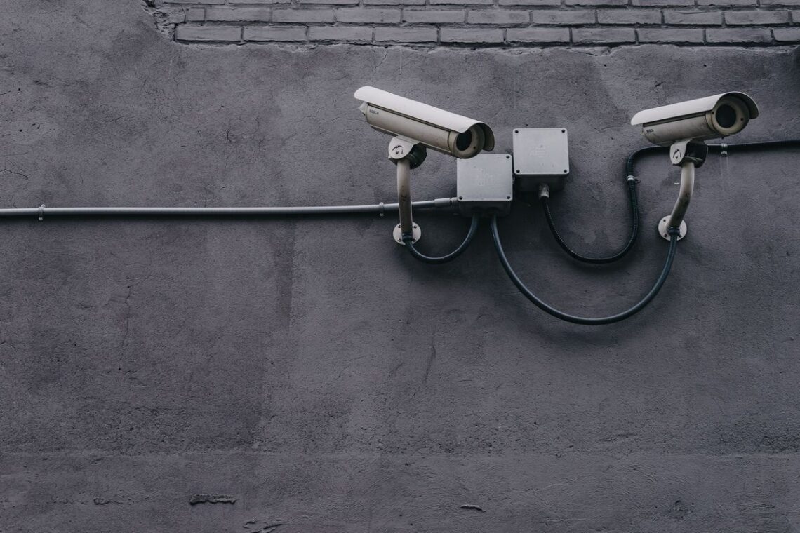 Two white security cameras mounted on a grey exterior wall with conduit boxes