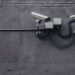 Two white security cameras mounted on a grey exterior wall with conduit boxes