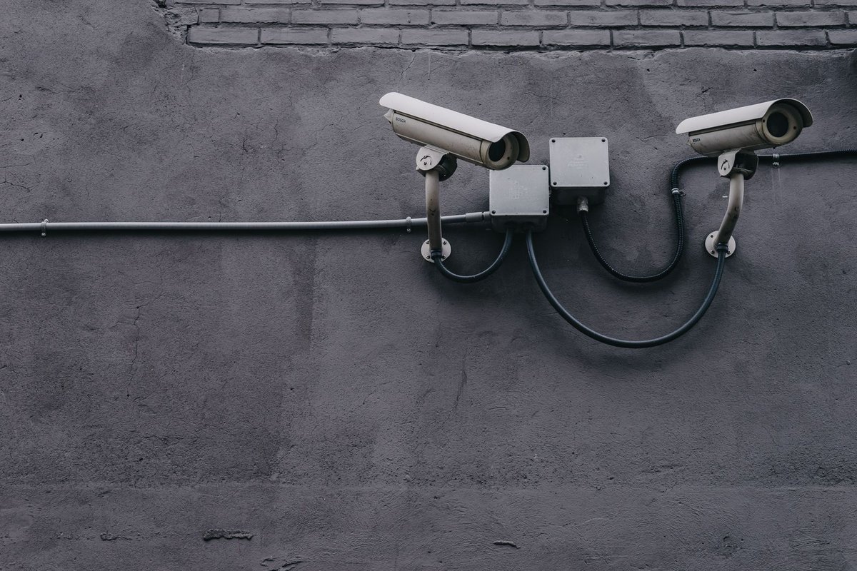 Two white security cameras mounted on a grey exterior wall with conduit boxes